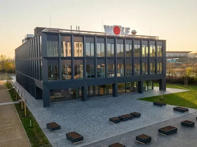 Außenansicht des WOLF CAMPUS in Mainburg mit moderner Glasfassade, Vorplatz und WOLF Logo auf dem Dach.