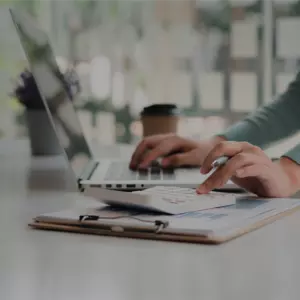 Eine Frau die neben ihrer Arbeit am Laptop mit den Taschenrechner etwas ausrechnet 