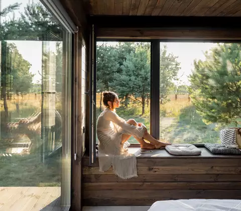 Eine Frau die im Wintergarten sitzt und die Sonne aus dem Fenster genießt 