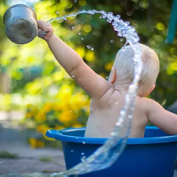 Ein Baby das in einem Wassereimer spielt und mit Wasser rum schlägt 