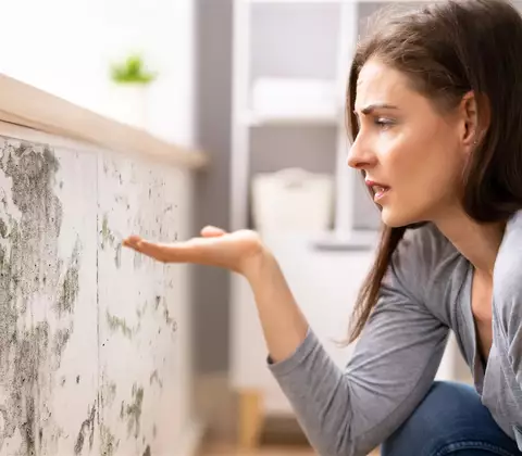 Frau kniet vor schimmelnder Wand