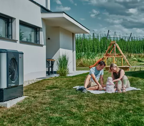 Familie mit Baby im Garten neben Wärmepumpe