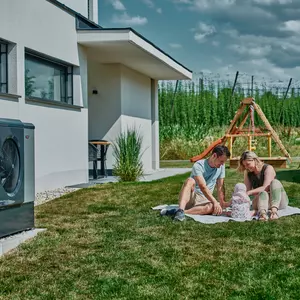 Familie mit Baby im Garten neben Wärmepumpe