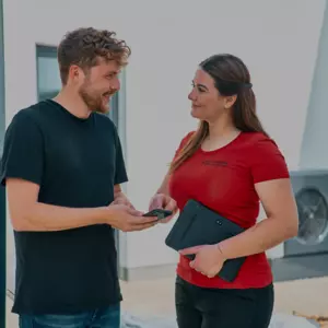 Fachhandwerker spricht mit Endkunde im Garten, im Hintergrund WOLF Wärmepumpe