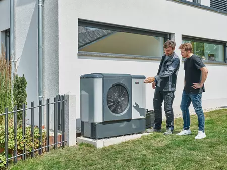 WOLF Mitarbeiter und Kunde betrachten Wärmepumpe im Garten