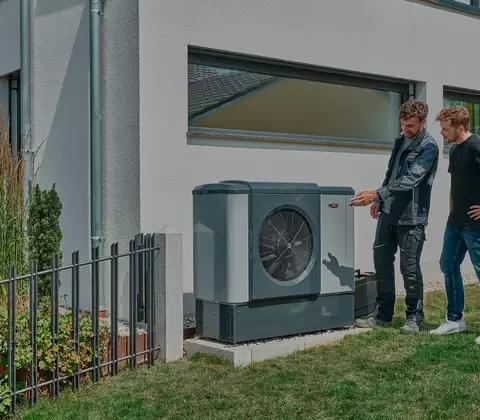 WOLF Mitarbeiter und Kunde betrachten Wärmepumpe im Garten